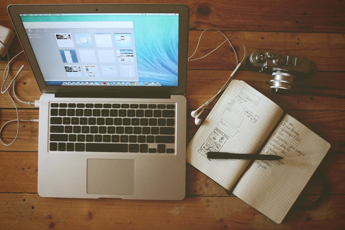 Laptop, camera, and notebook with web design sketches on a wooden desk